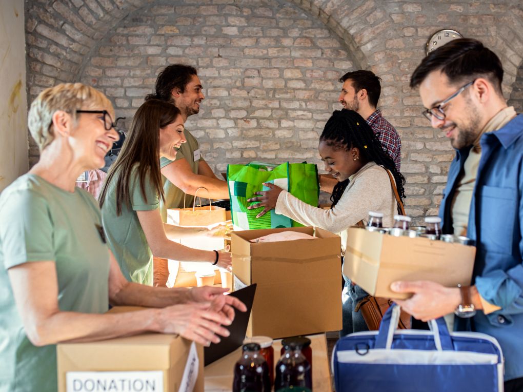 Group of diverse volunteers happily organizing and distributing donation boxes and food supplies at a community center, showcasing teamwork and charitable giving.