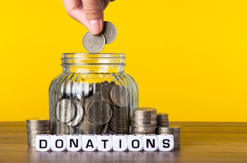 hand placing coins into a donation jar symbolizing charitable giving and the concept of Gift Aid in the UK, including charity Gift Aid and Gift Aid grants