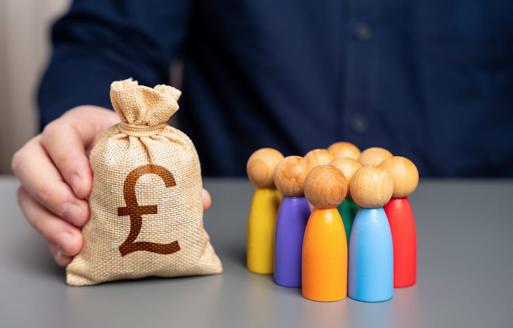 A businessman holds a british pound sterling money bag near a group of people figurines to explain successful online fundraising campaigns